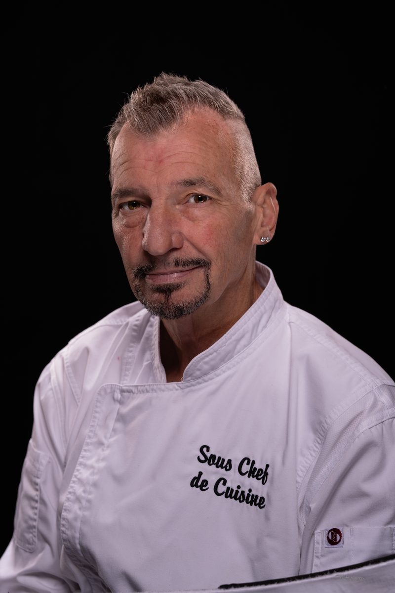 Studio headshot of a chef in whites on a black background
