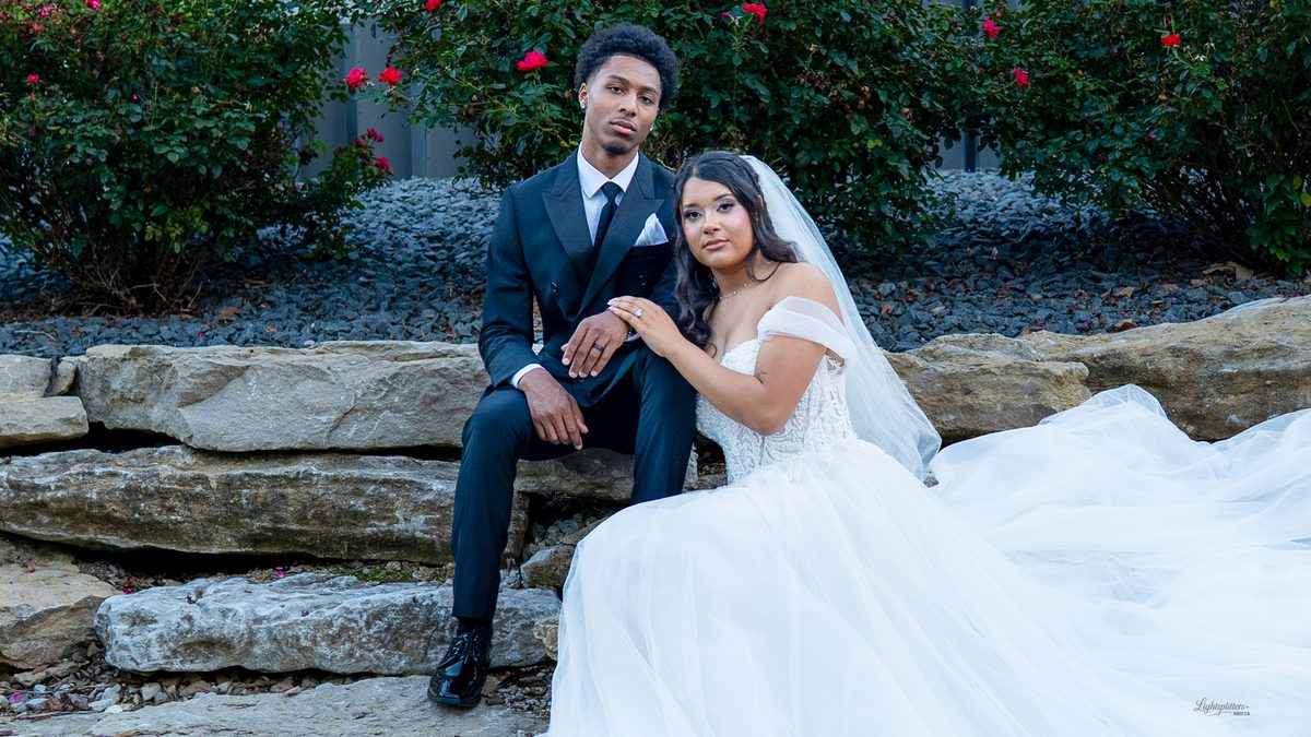 Bride and groom seated on a stone ledge, her train spread across the rocks